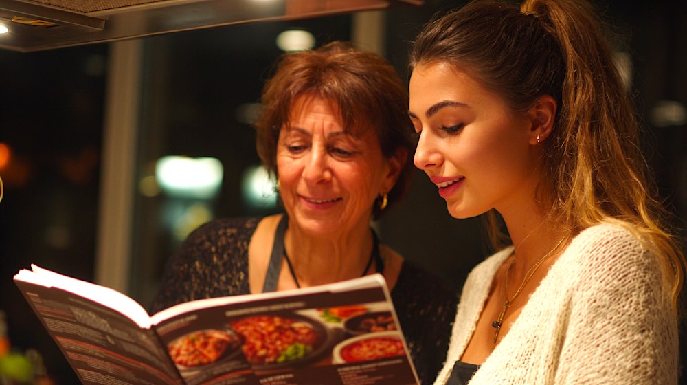 Twee vrouwen kijken naar kookboek in een keuken.