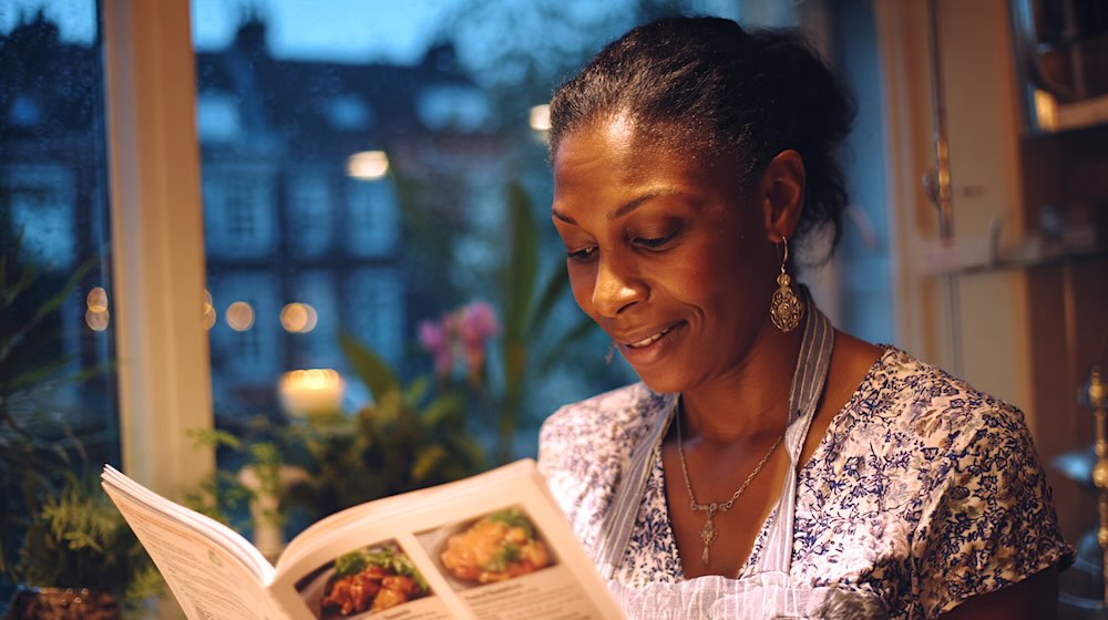 Vrouw leest kookboek in keuken met planten en Amsterdam op de achtergrond