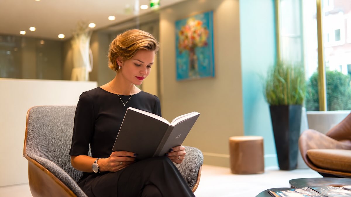 in de receptie van een bedrijf leest een blonde vrouw met rode lipstick een boek in b5 formaat